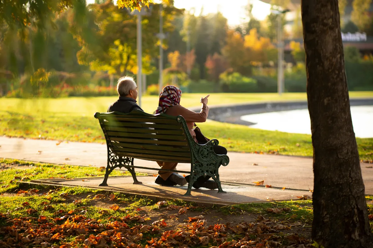 A couple sitting together on a park bench in a leafy village garden